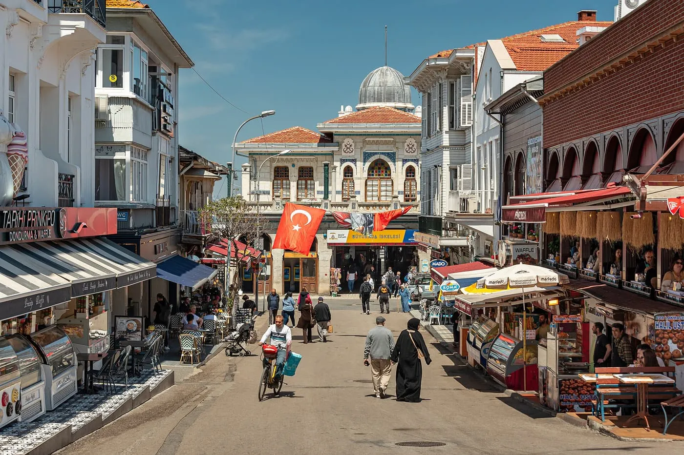 The pedestrian square by the ferry landing on Büyükada, with café tables, wooden houses and a domed pavilion