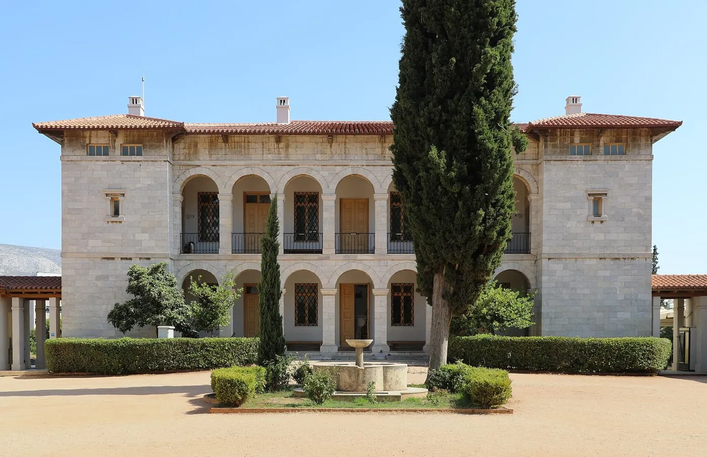 The stone villa of the Byzantine and Christian Museum, with two tiers of arches, a cypress tree and a small fountain in the gravel courtyard