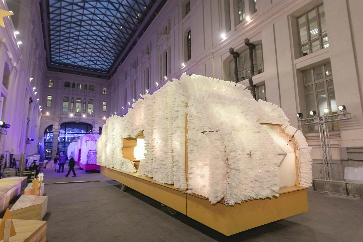 A parade float covered in rolled white paper standing in the glass-roofed courtyard of the Palacio de Cibeles