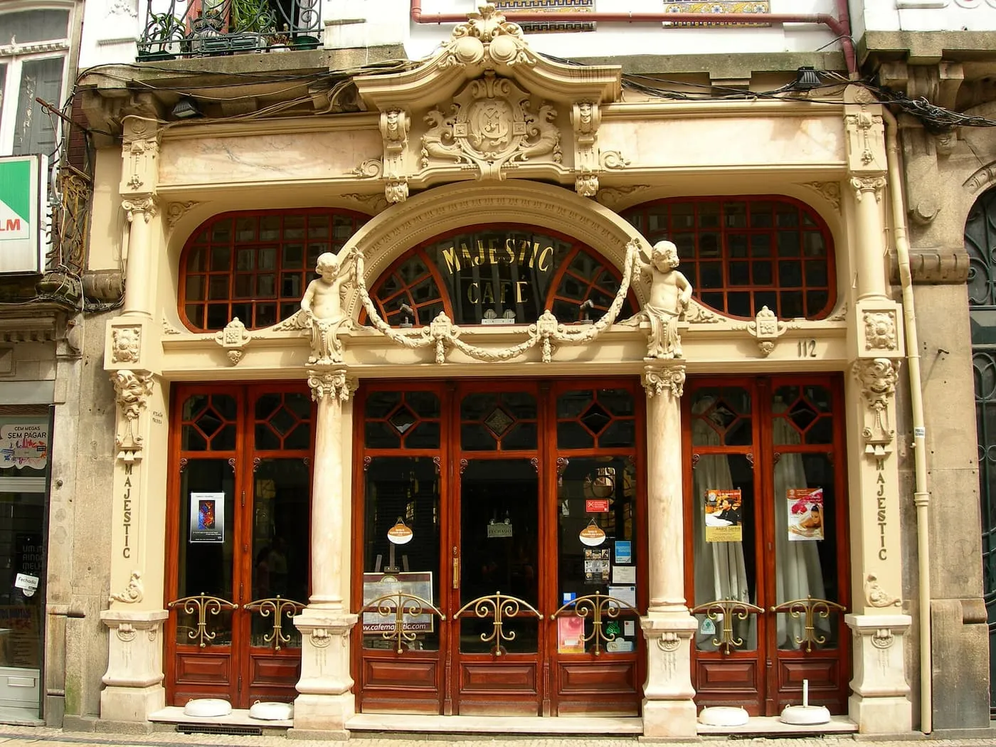 The carved cream façade of the Café Majestic, with its arched sign held by two stone cherubs above red-framed doors