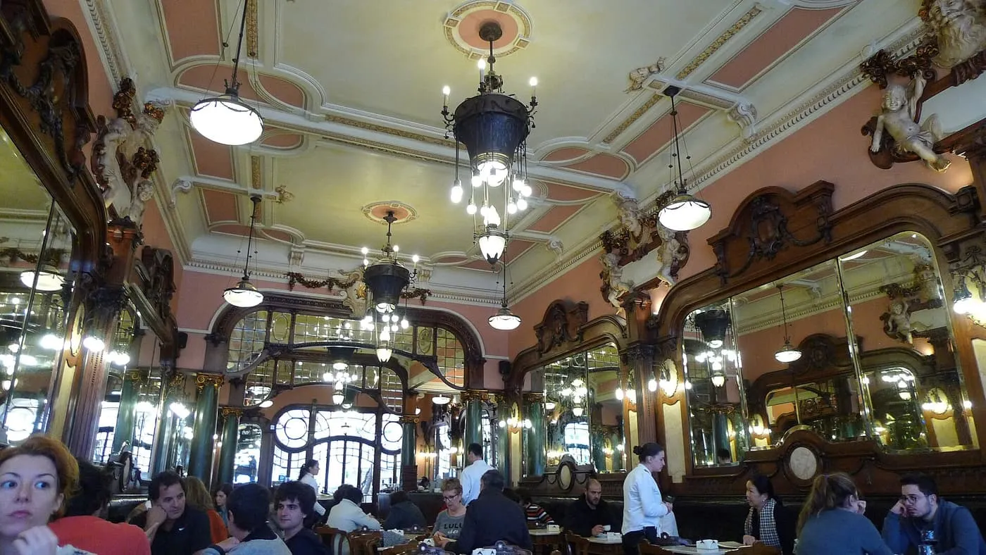 The panelled room of the Café Majestic, with carved wood, mirrors, pink walls, plaster cherubs and chandeliers above diners at their tables