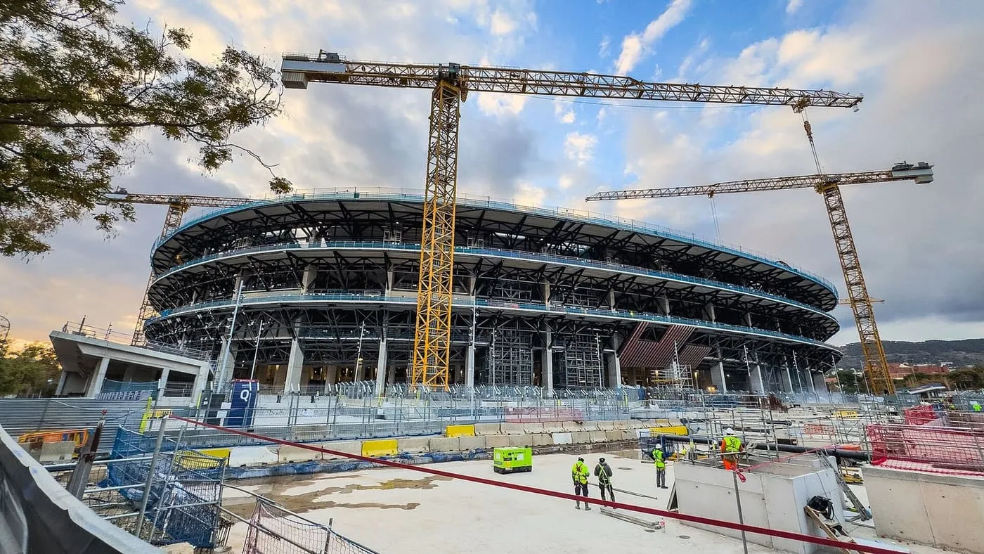 The steel frame of the Spotify Camp Nou's new tiers under construction, with three yellow tower cranes and workers in high-visibility jackets in the foreground
