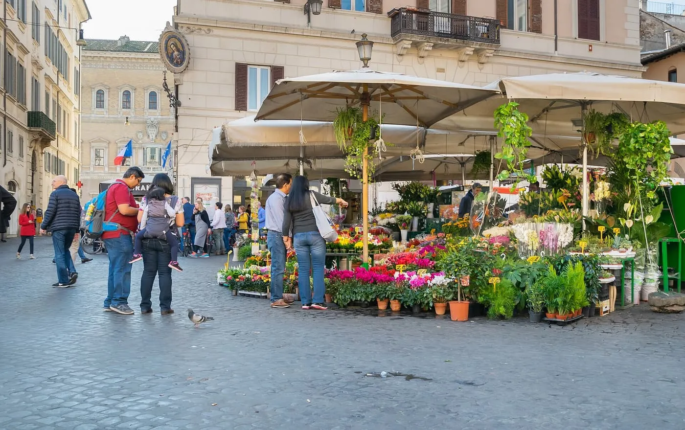 A flower stall under cream umbrellas on Campo de' Fiori, with shoppers on the cobbles