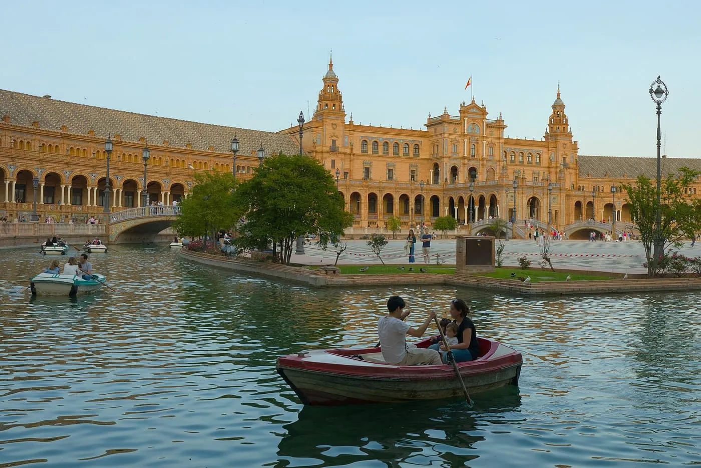 A rowing boat on the canal in front of the central building of the Plaza de España, with other boats and the curved arcade beyond