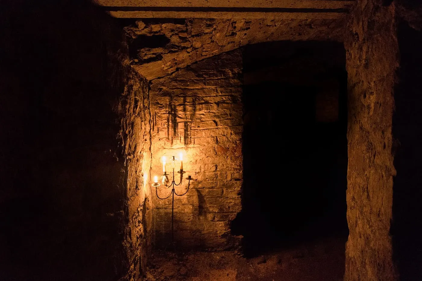A stone-walled underground vault lit by a single candelabra, with a dark passage beyond