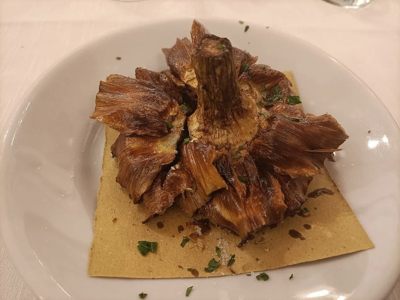 A whole artichoke fried flat, with the outer leaves opened like petals, on a plate