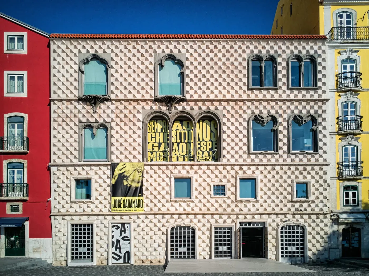 The front of the Casa dos Bicos, covered in rows of diamond-shaped stone points, with pointed windows and a banner on the first floor