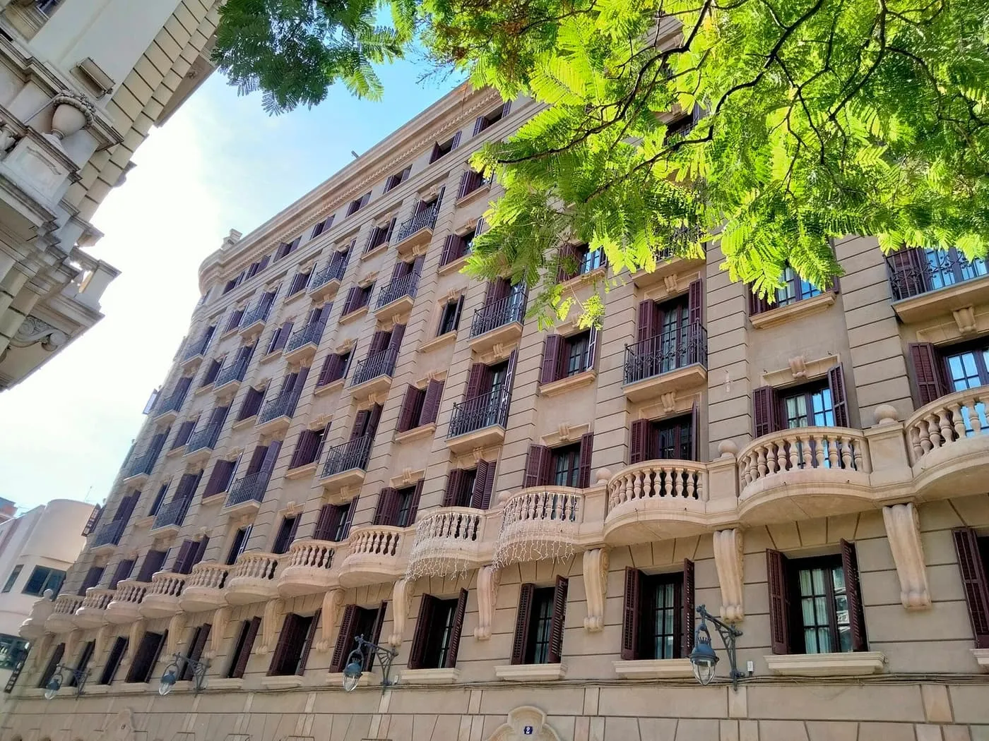 The cream stone façade of Casa Manuel Barguñó, seen from below, with rows of shuttered windows and balconies under a tree