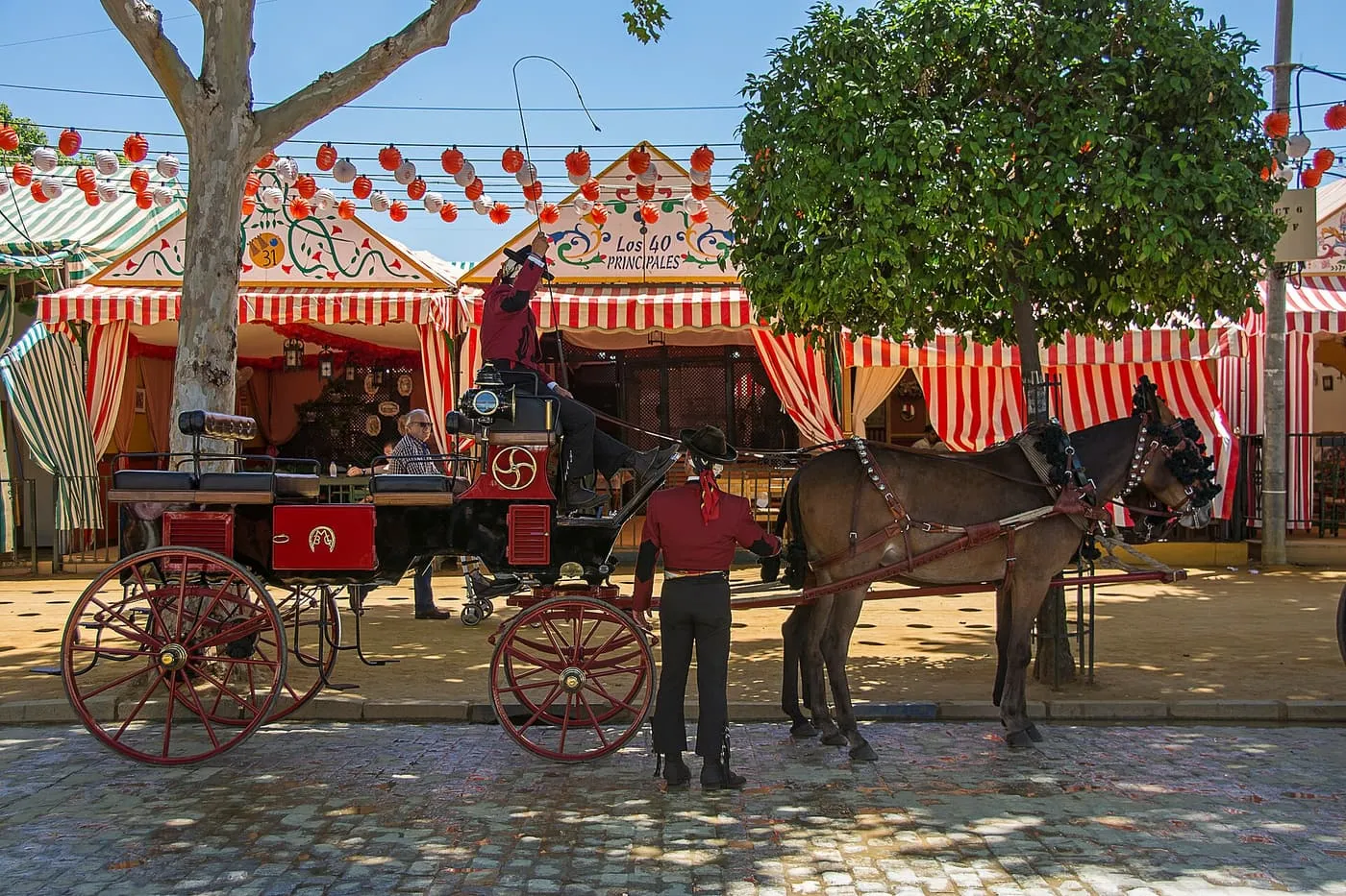 A horse-drawn carriage in front of red and white striped casetas hung with paper lanterns