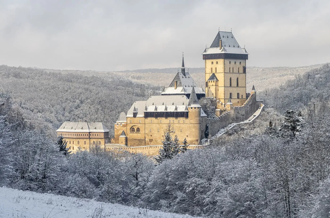 Karlštejn Castle and its Great Tower among snow-covered woods, seen from across the valley