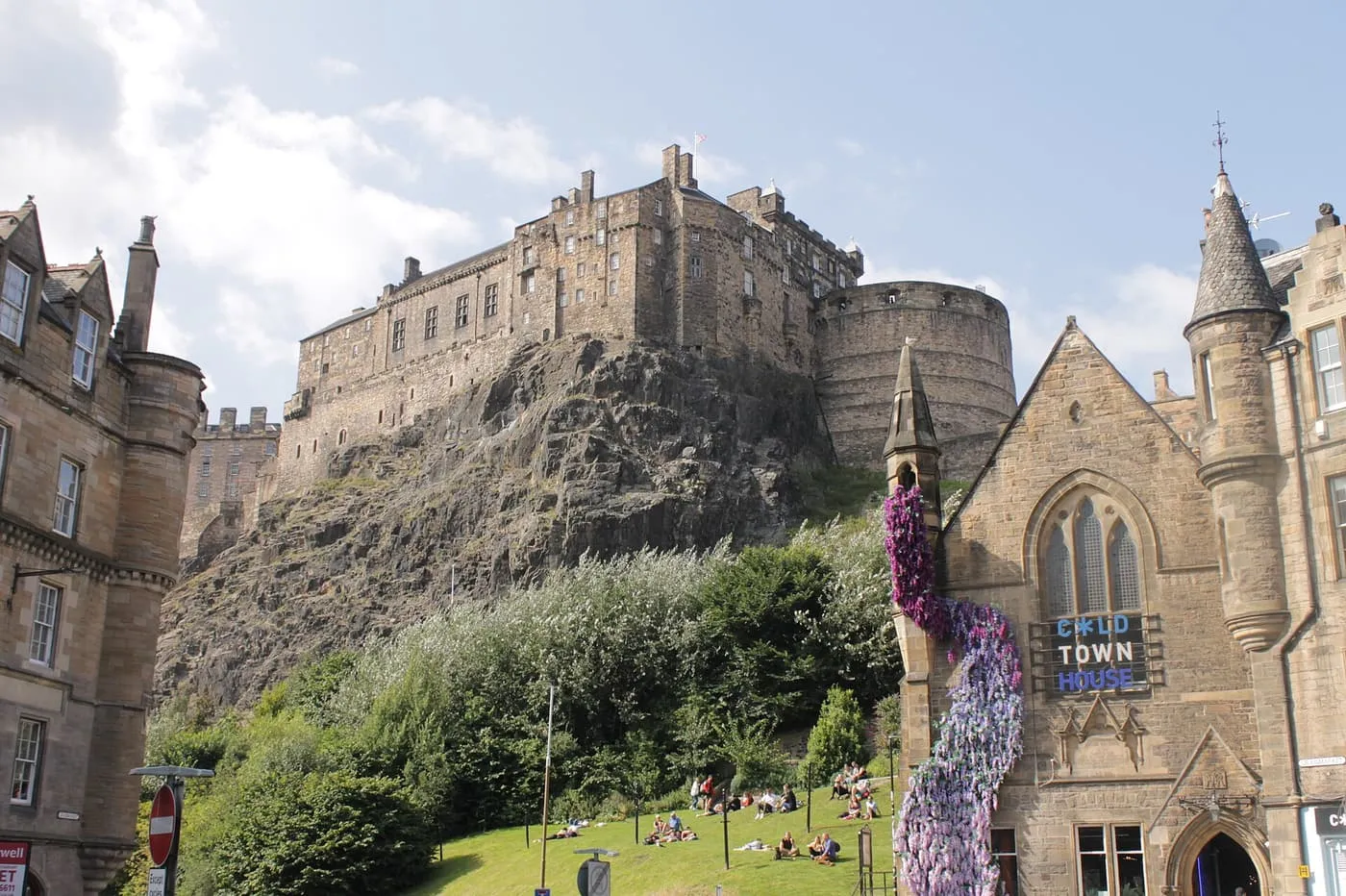Edinburgh Castle on its rock above a green slope beside the Grassmarket, with people sitting on the grass