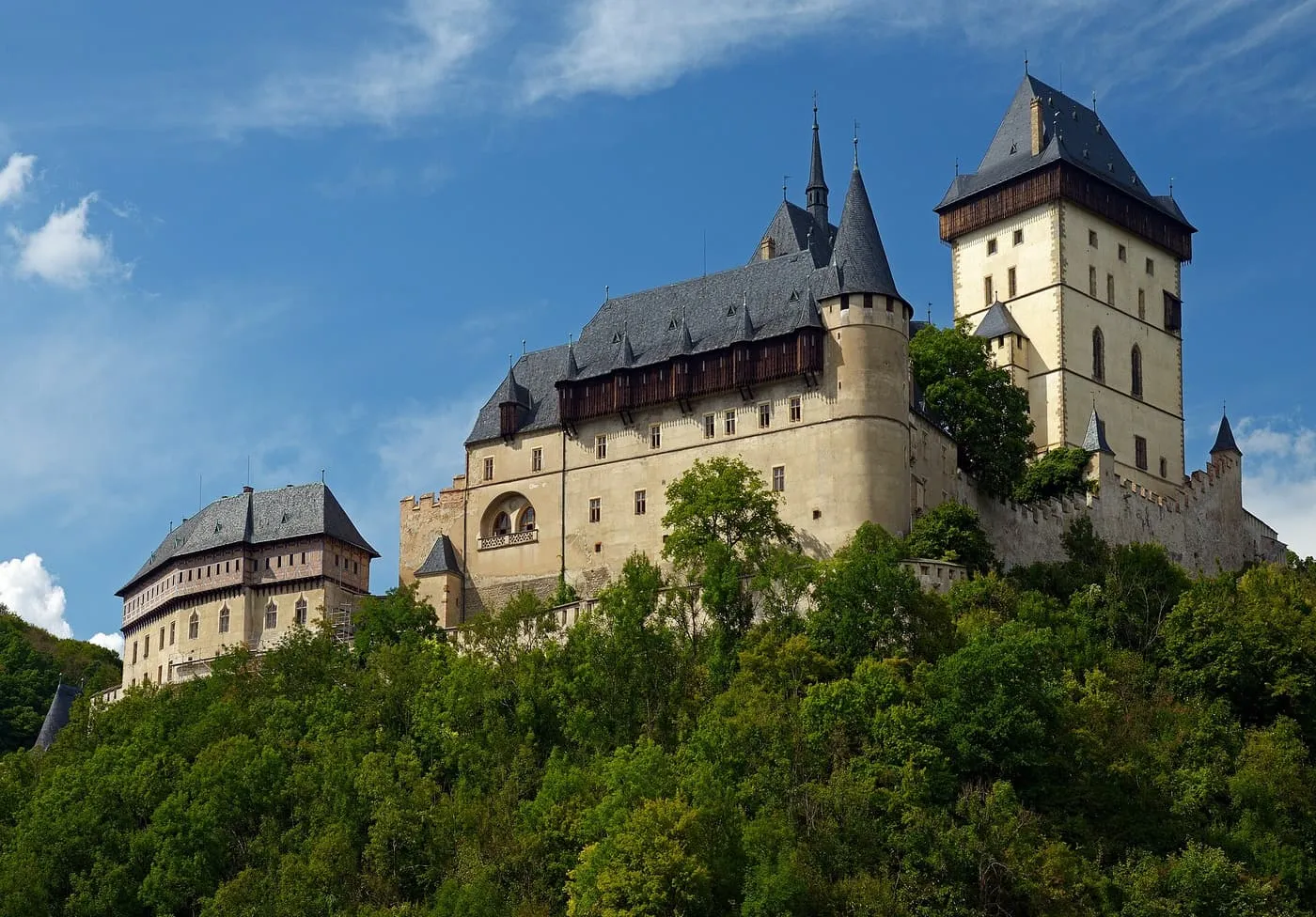 Karlštejn Castle on its wooded hill, with the tall Great Tower on the right and the pale stone walls and dark slate roofs of the palace below it