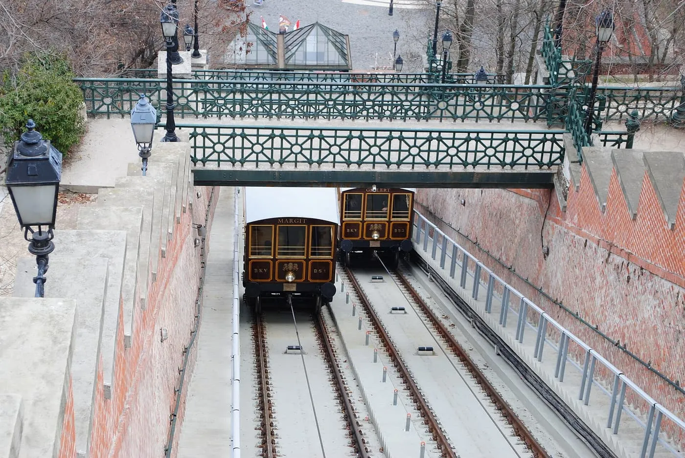 Two wooden cable cars passing on the Castle Hill Funicular's twin tracks, beneath a green iron footbridge