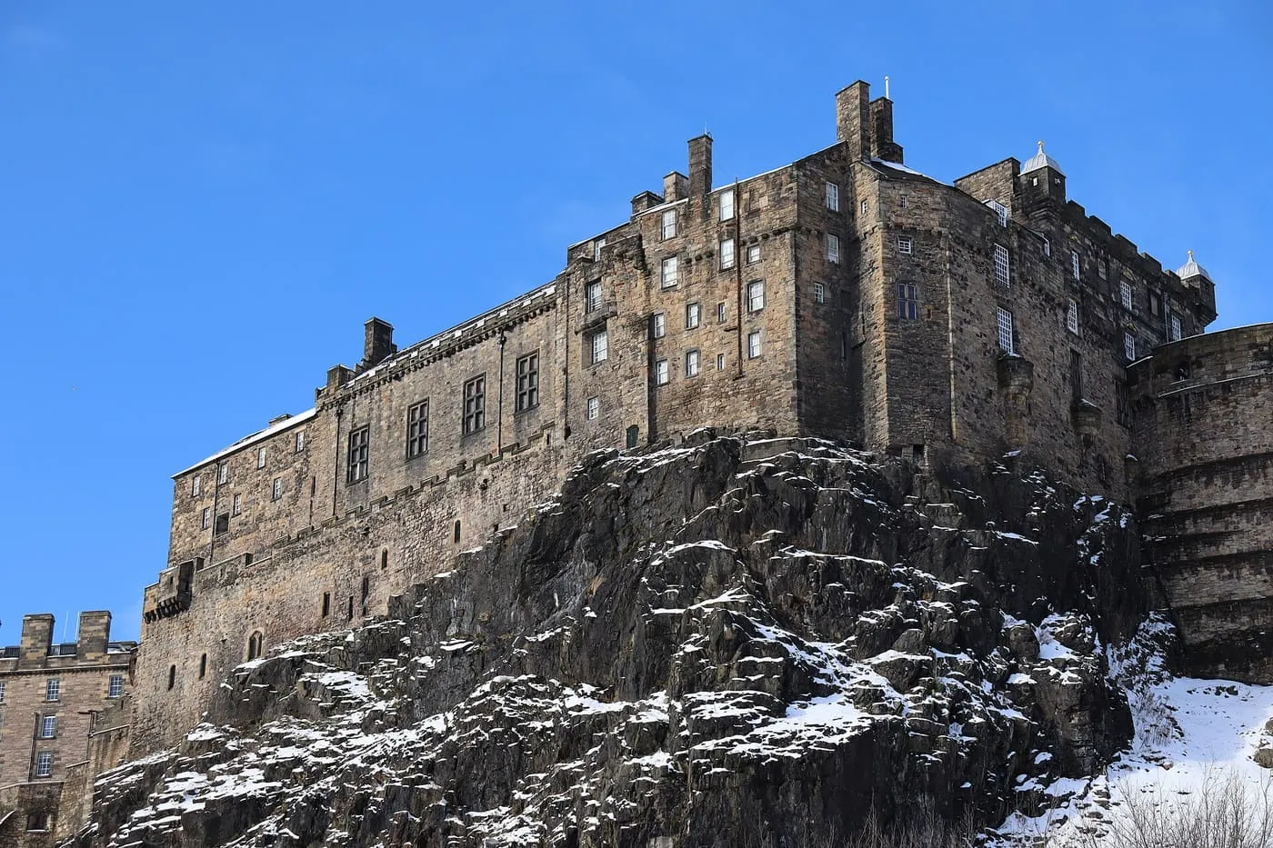 The south side of Edinburgh Castle on its crag, with snow lying on the rock under a clear blue sky