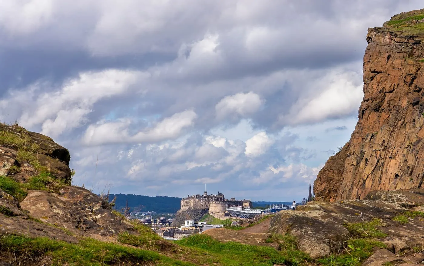 Edinburgh Castle in the distance, framed between a rock face of Salisbury Crags and a rocky foreground