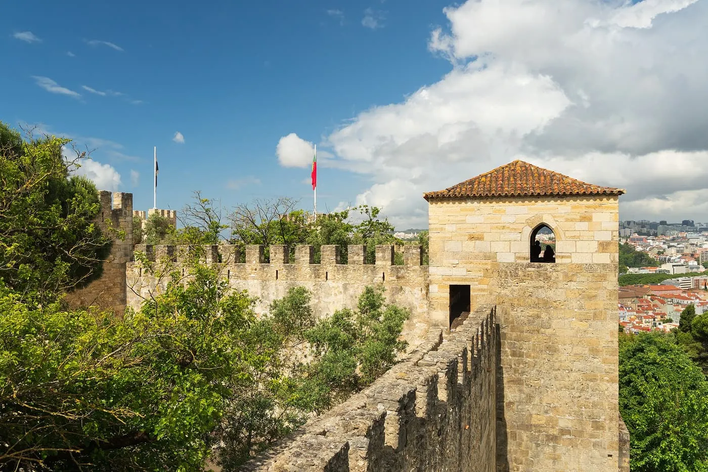 A battlemented wall and a tiled-roof tower of the Castelo de São Jorge, with Lisbon's roofs beyond