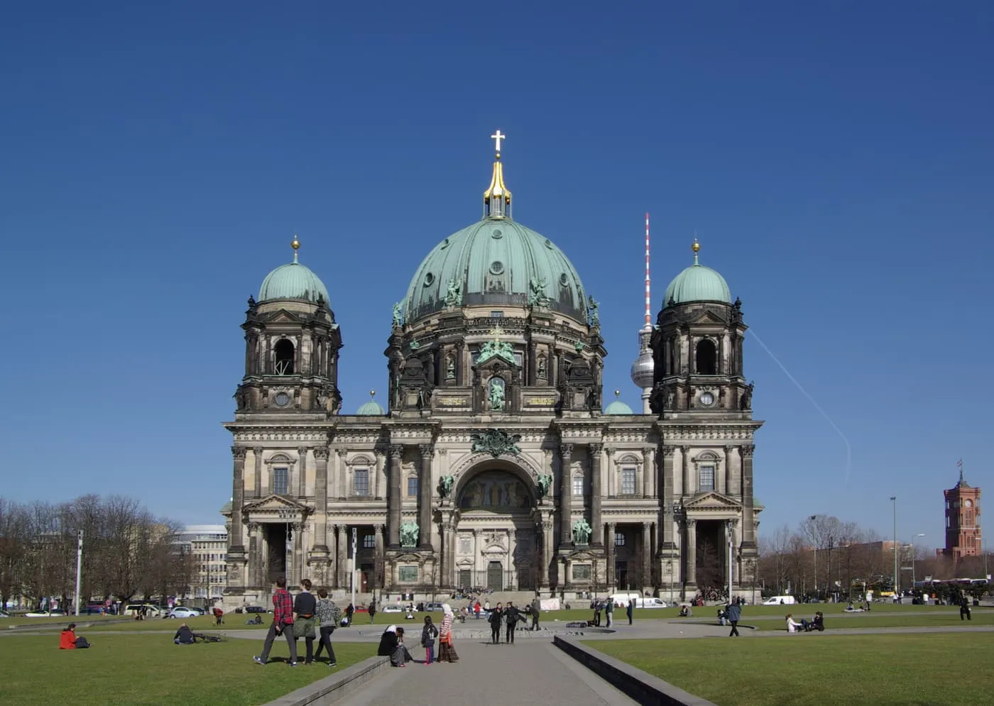 The Berlin Cathedral with its green copper dome and two flanking towers, seen across the grass of the Lustgarten with the TV Tower behind