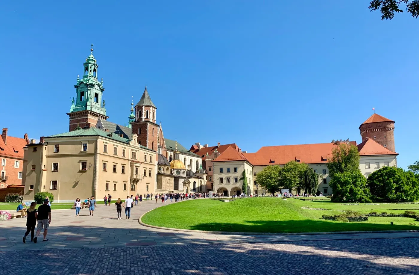 Wawel Cathedral with its green-capped tower and golden chapel dome, beside the Castle buildings and a lawn on the hilltop