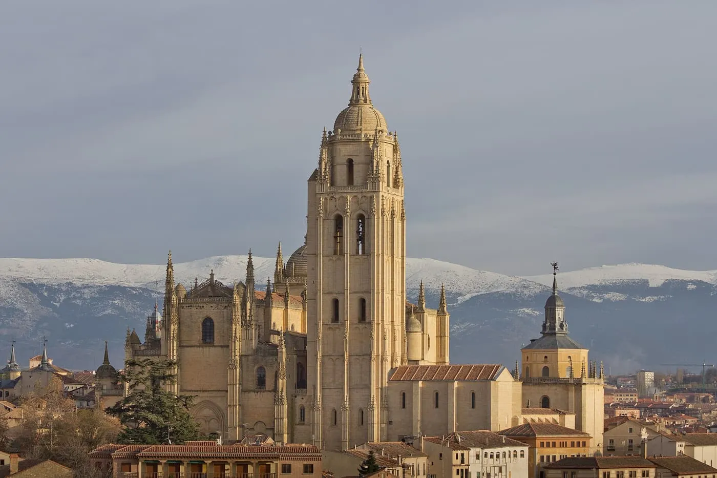 The Cathedral of Segovia with its tall bell tower and pinnacled walls, the snow-covered Sierra de Guadarrama behind