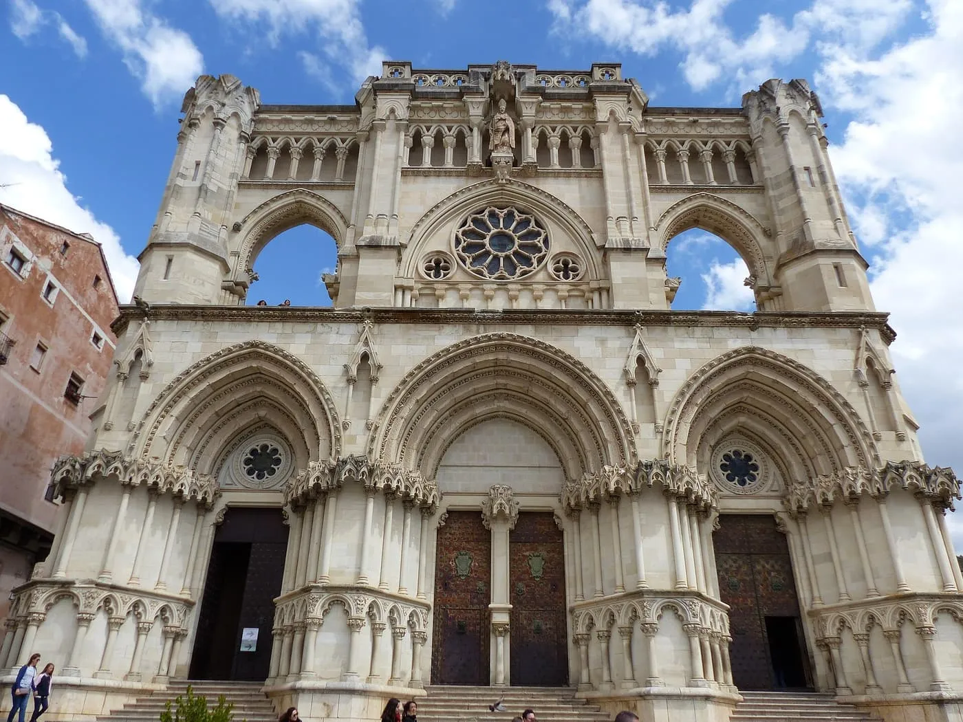The pale stone Gothic façade of Cuenca Cathedral, with three pointed doorways, a rose window and open arches above