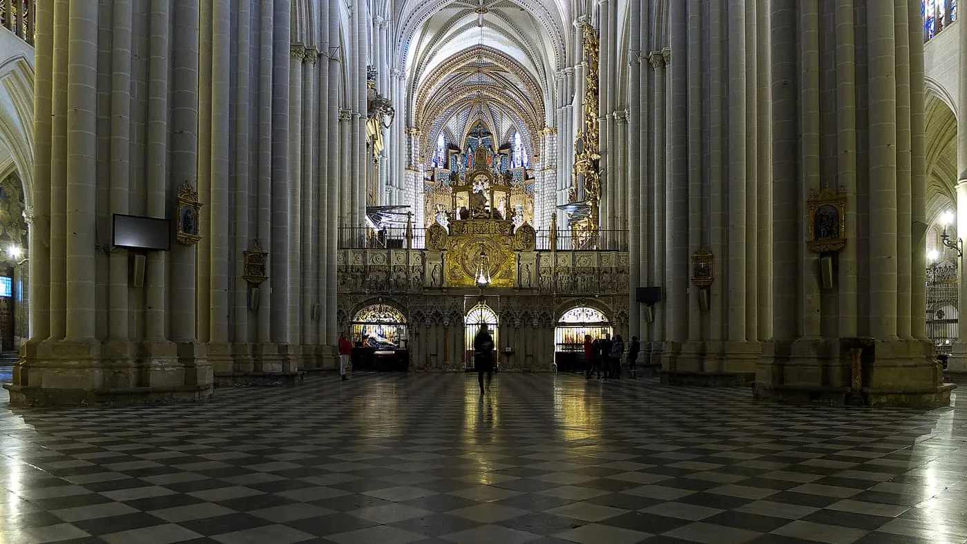 The nave of Toledo Cathedral looking towards the gilded Main Chapel, with tall clustered columns and a black and white marble floor
