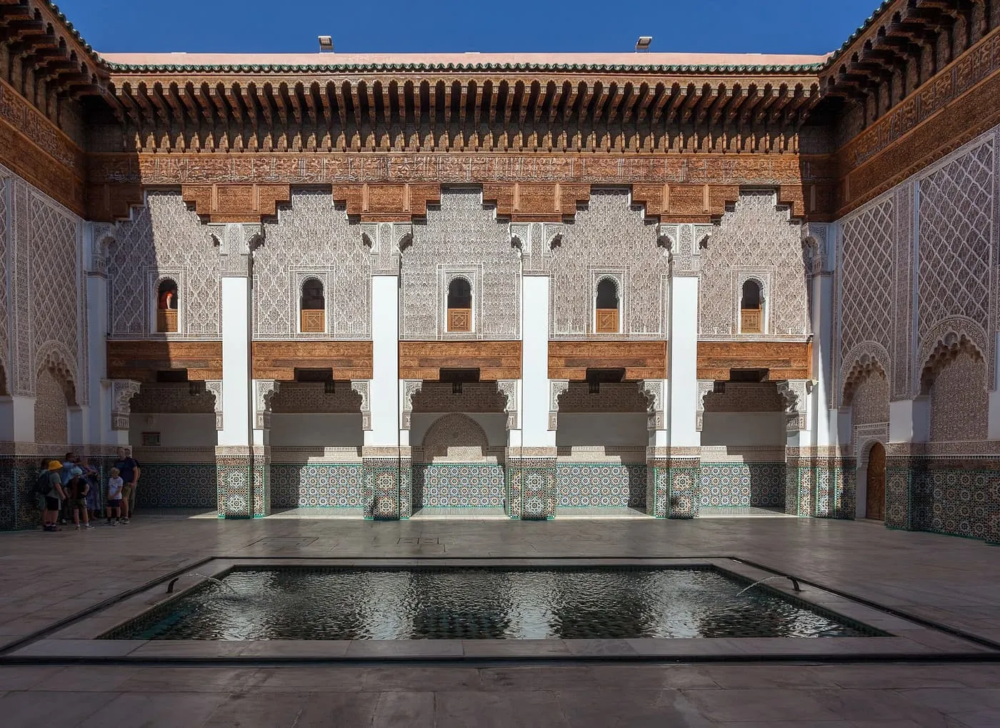 The central courtyard of the Ben Youssef Madrasa, with a rectangular pool in front of galleries of carved plaster, carved cedar and tilework