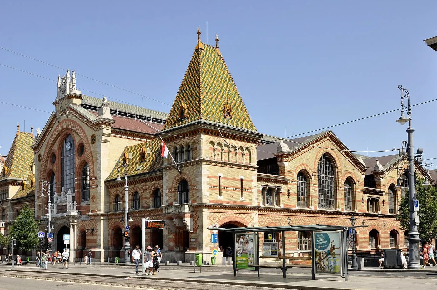 The Central Market Hall, with its tiled pyramid roof and brick and stone front, beside a tram stop