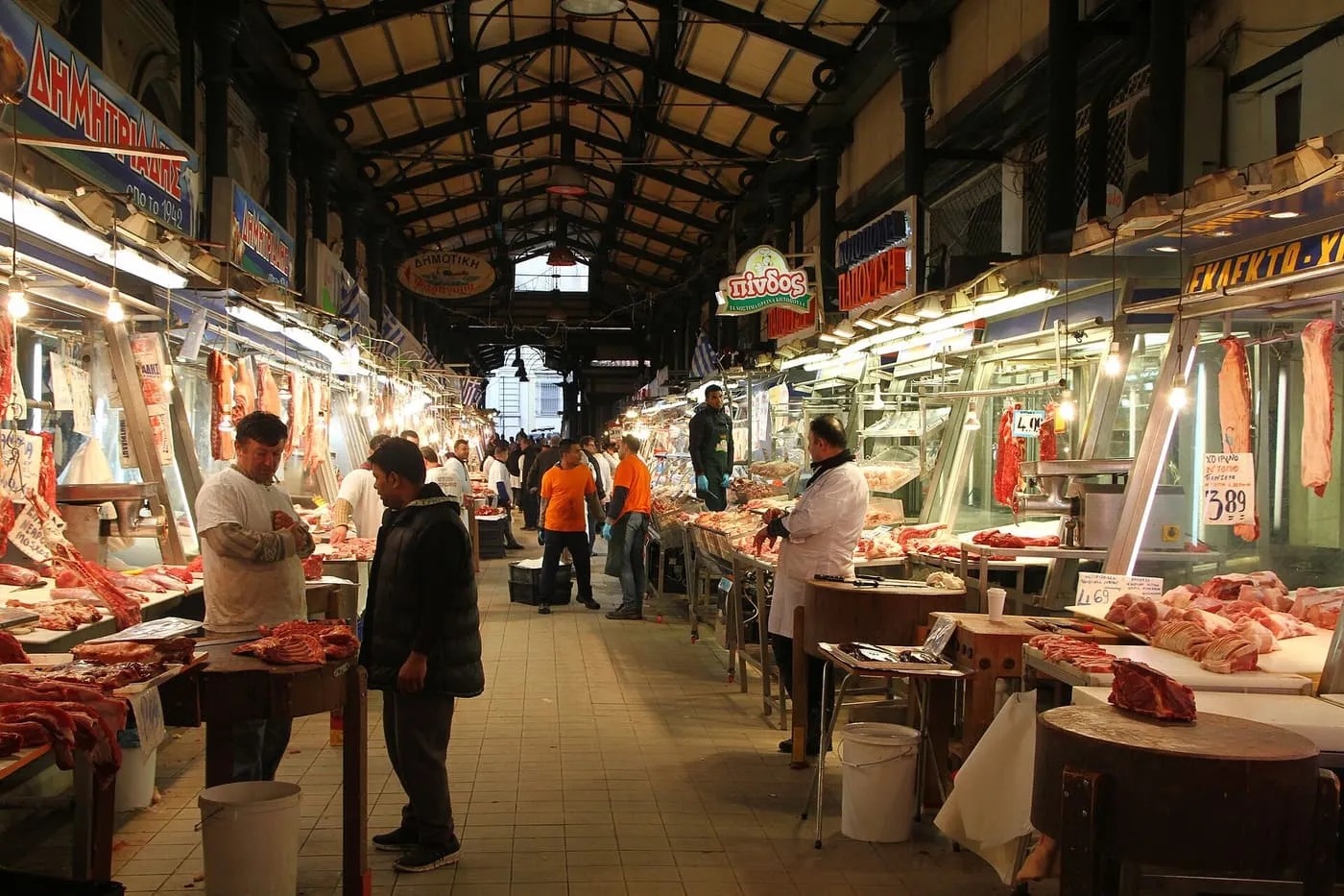 The meat hall of the Varvakios Central Market under its iron roof, with butchers behind glass counters and shoppers walking the central aisle