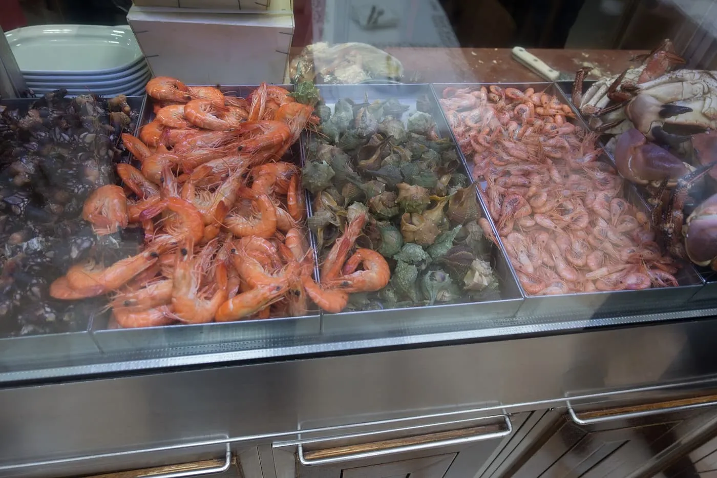 Trays of cooked prawns, whelks, small shrimp and brown crab behind glass at Cervejaria Ramiro