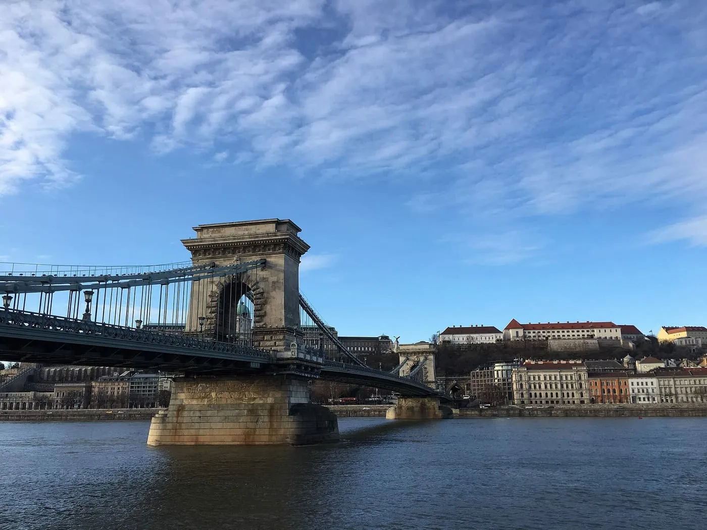 The Széchenyi Chain Bridge's stone tower and deck across the Danube, with Castle Hill buildings on the Buda bank