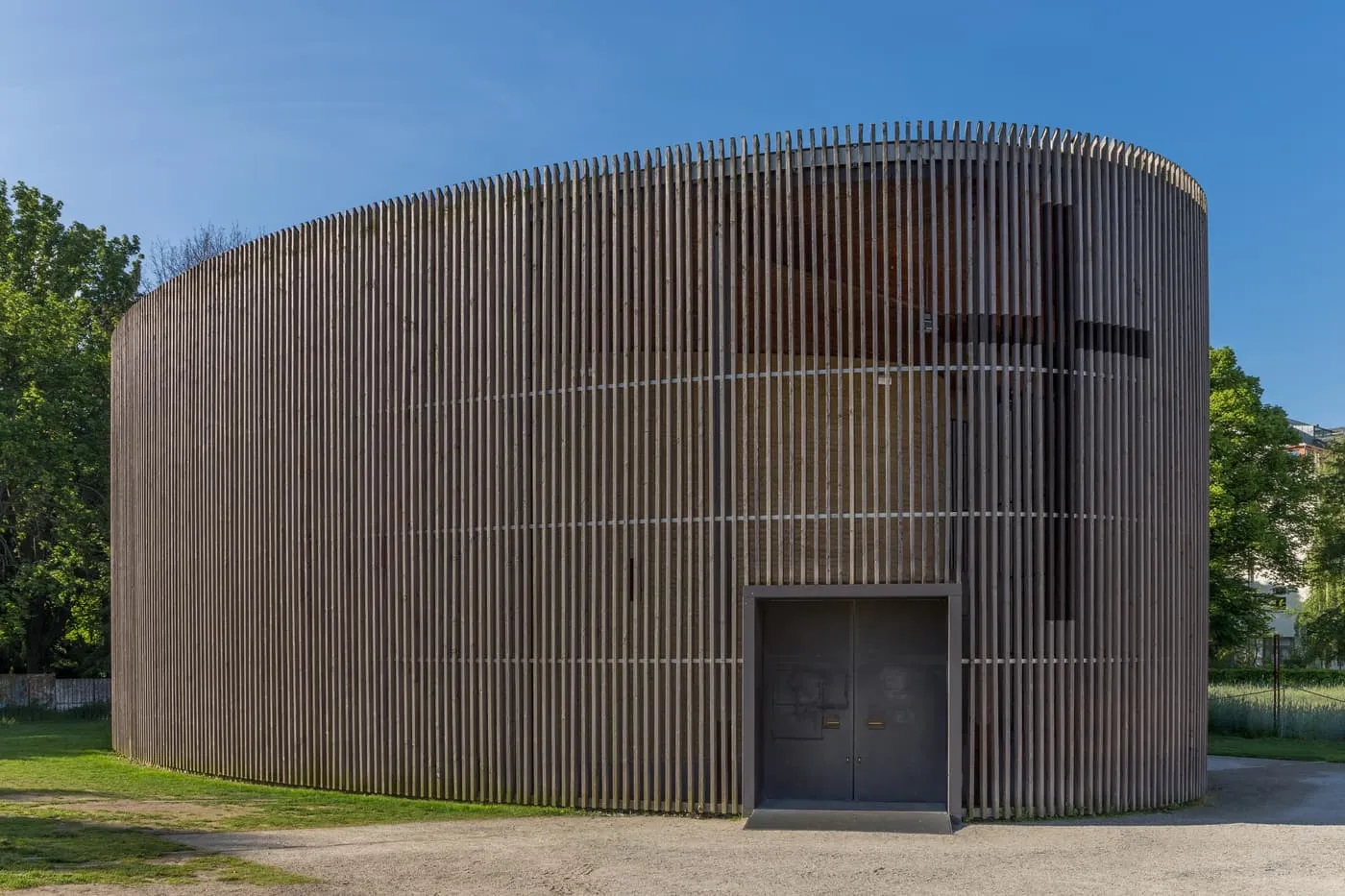 The Chapel of Reconciliation, an oval building clad in vertical timber slats, with a dark door and a cross cut into the cladding