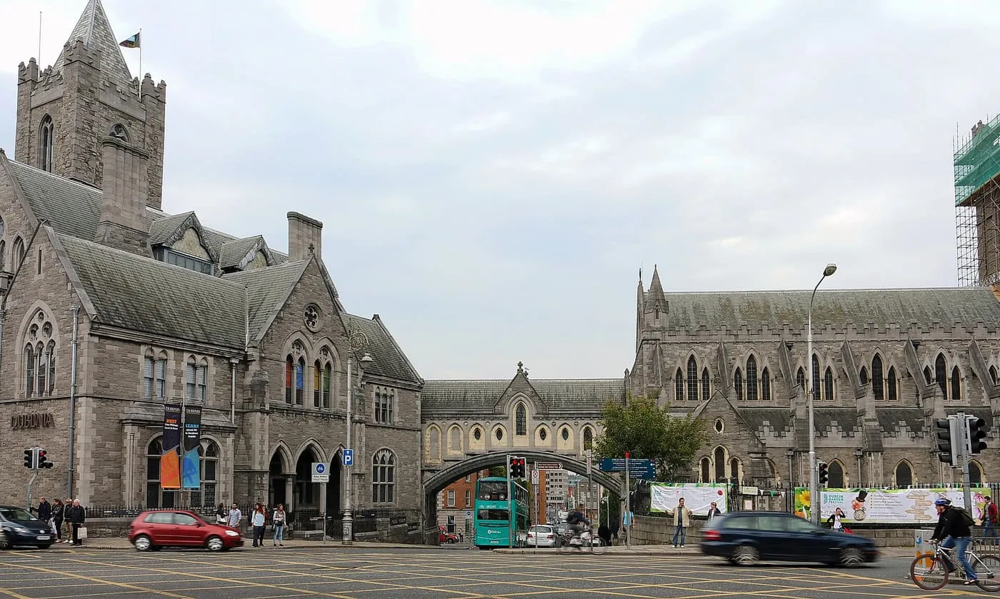 Christ Church Cathedral and the Synod Hall joined by a stone bridge across the street, seen from the road with traffic passing