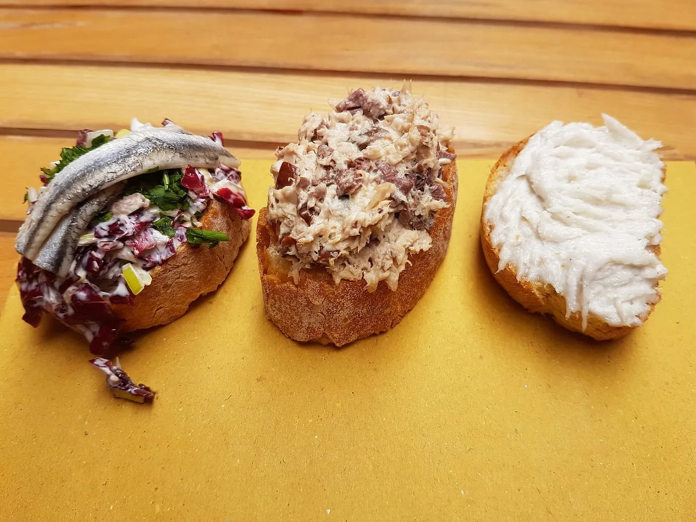 Three cicchetti on slices of bread: anchovy on radicchio, beans and tuna, and creamed salt cod