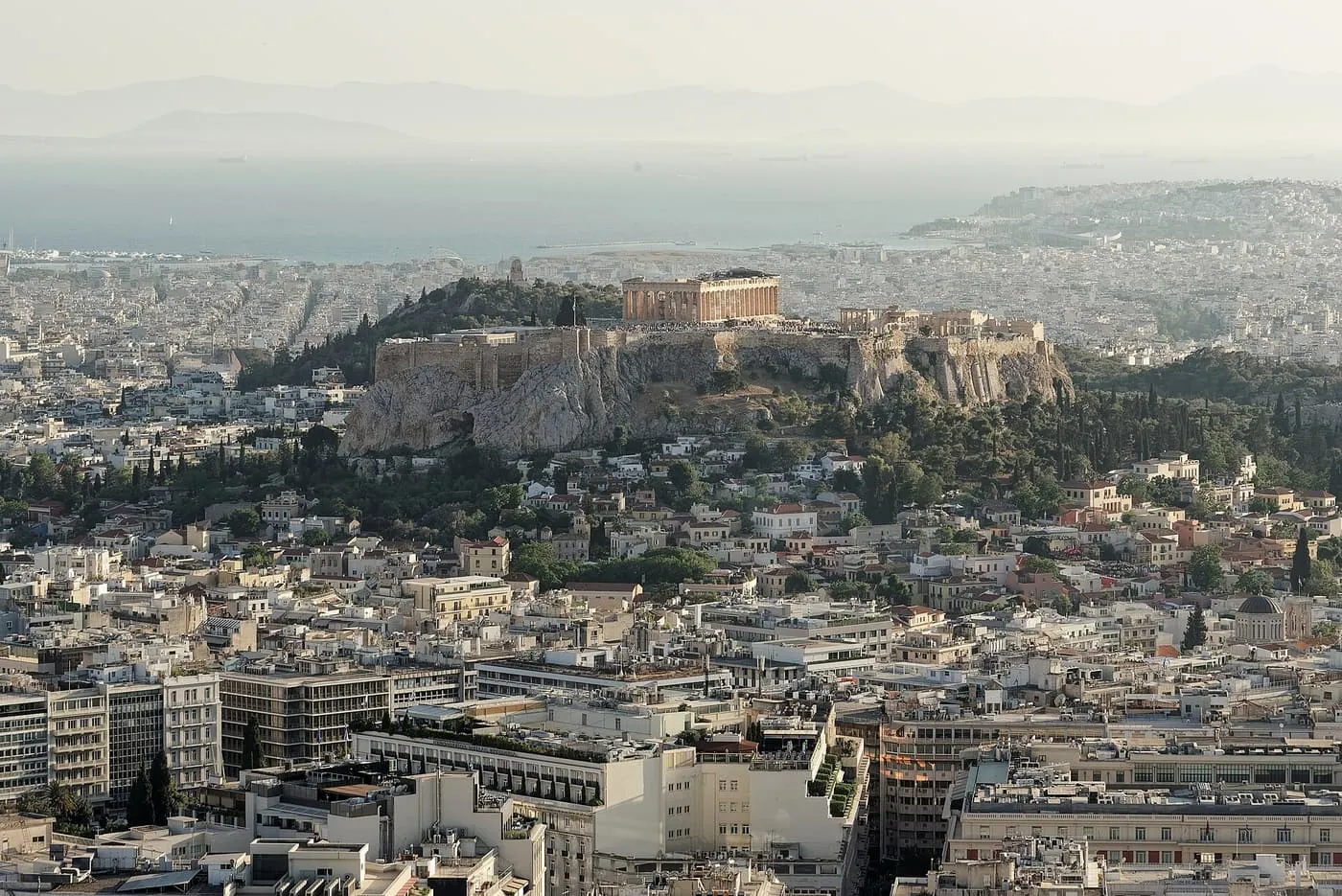 The Acropolis and the Parthenon rising above the roofs of central Athens, with the sea and the coast behind, seen from the top of Lycabettus