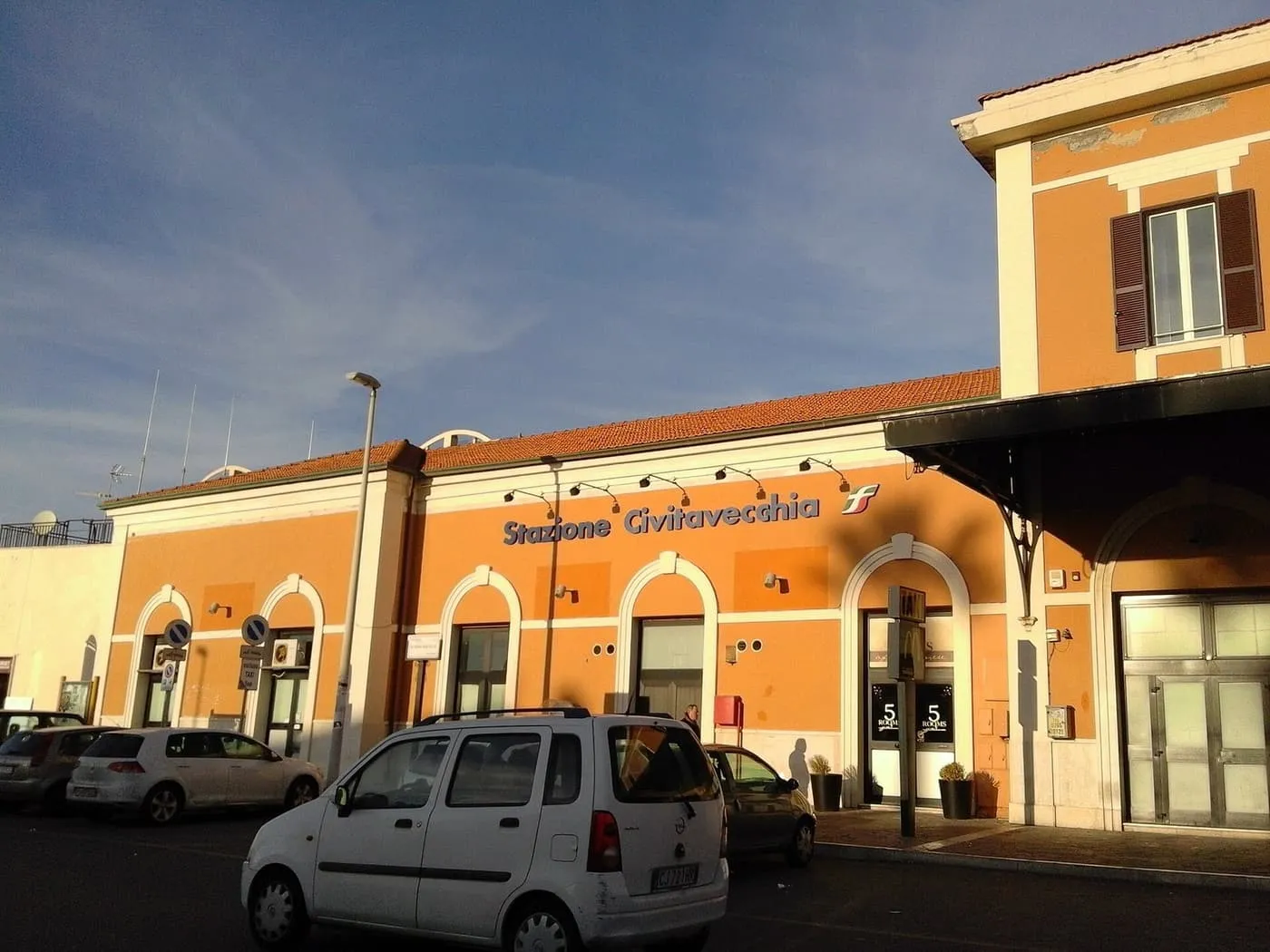 The orange front of Civitavecchia station, with the station name across it and cars parked outside