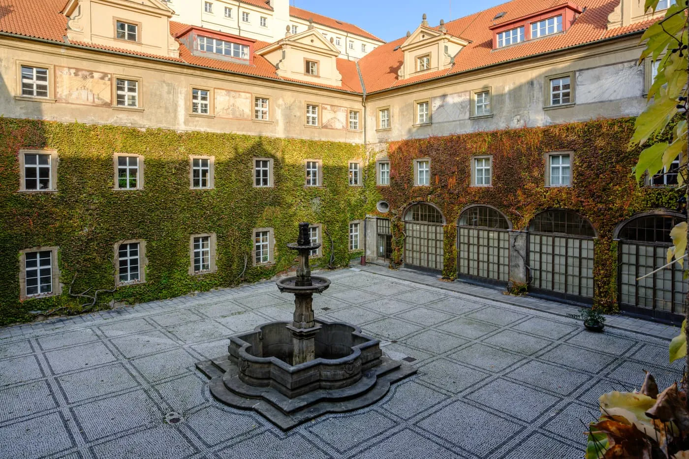 A cobbled courtyard with a stone fountain and ivy-covered walls in the Clementinum