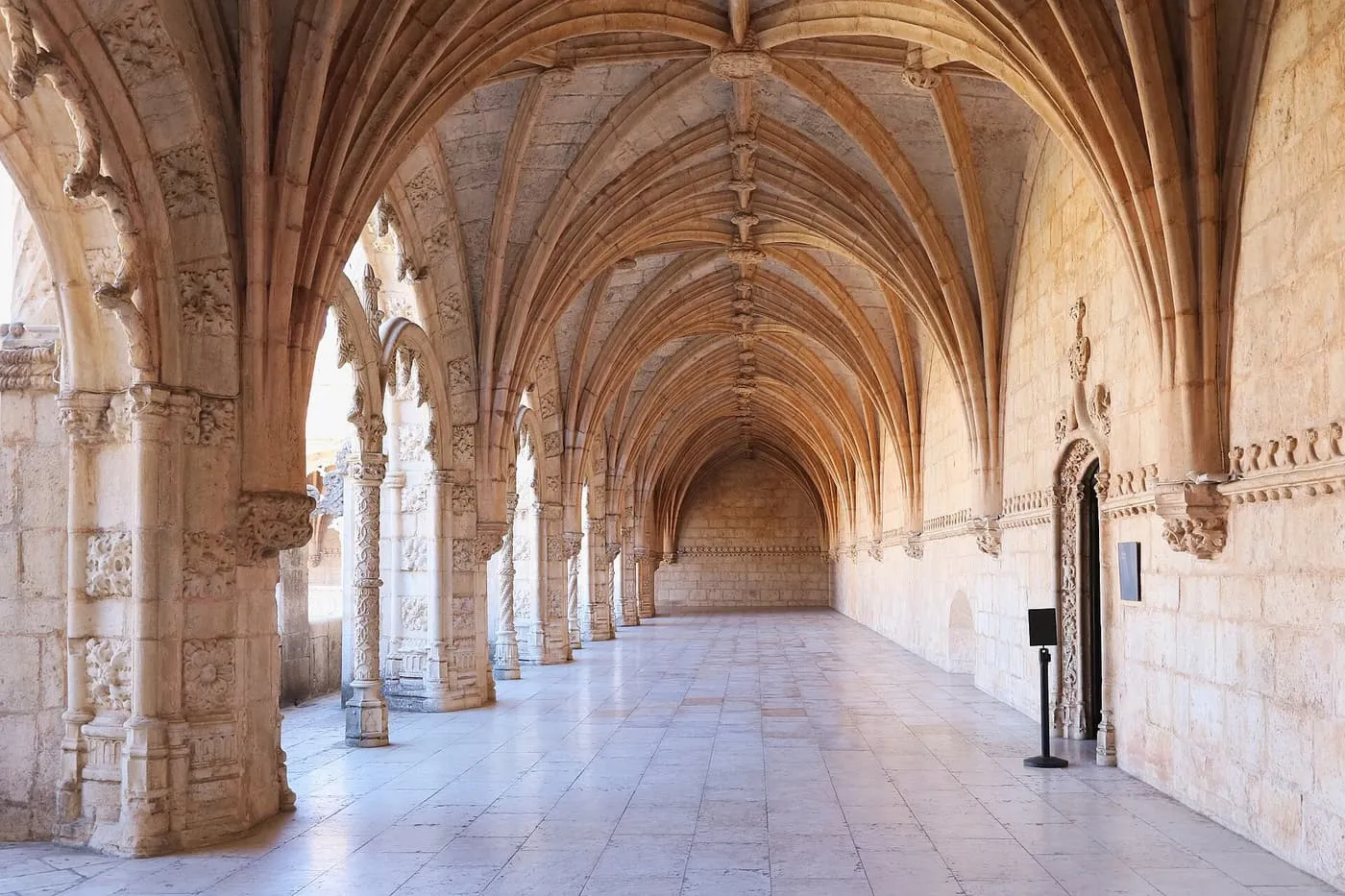 A vaulted stone gallery of the Jerónimos cloister, with carved arcades on the left