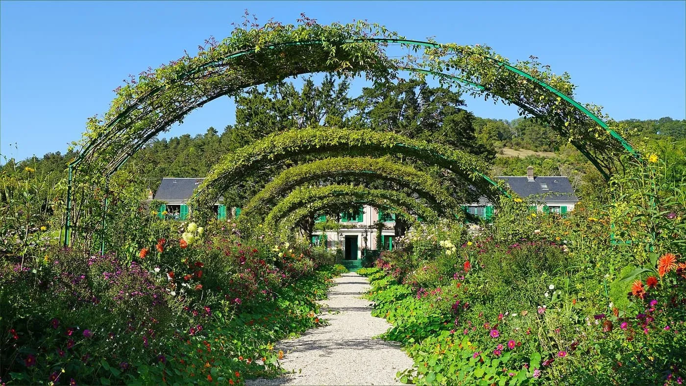 Rose arches over the gravel main path of the Clos Normand, with Monet's house and its green shutters at the far end
