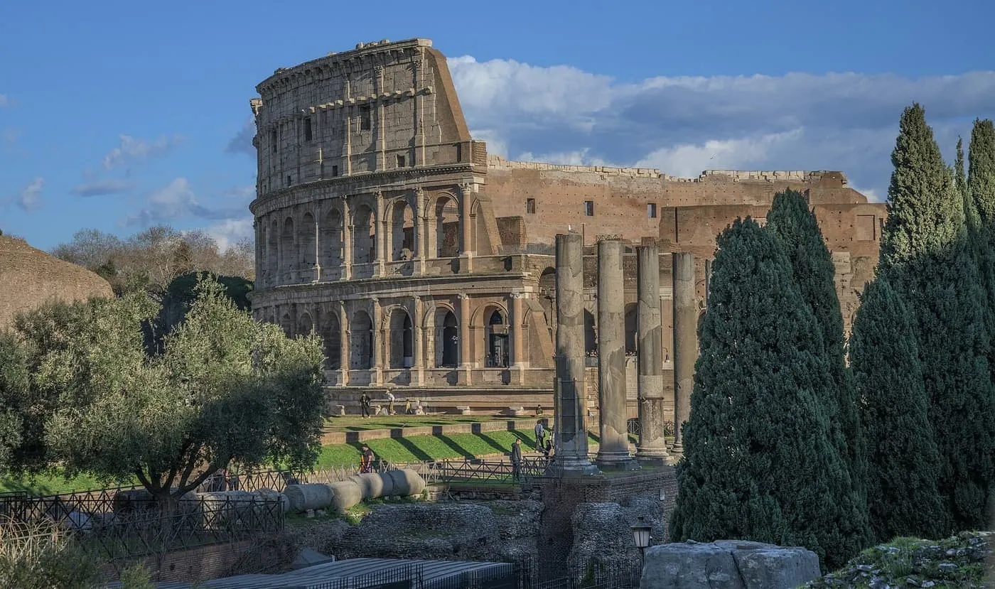 The Colosseum seen past the ruins of the Roman Forum, with cypress trees and a row of columns in the foreground