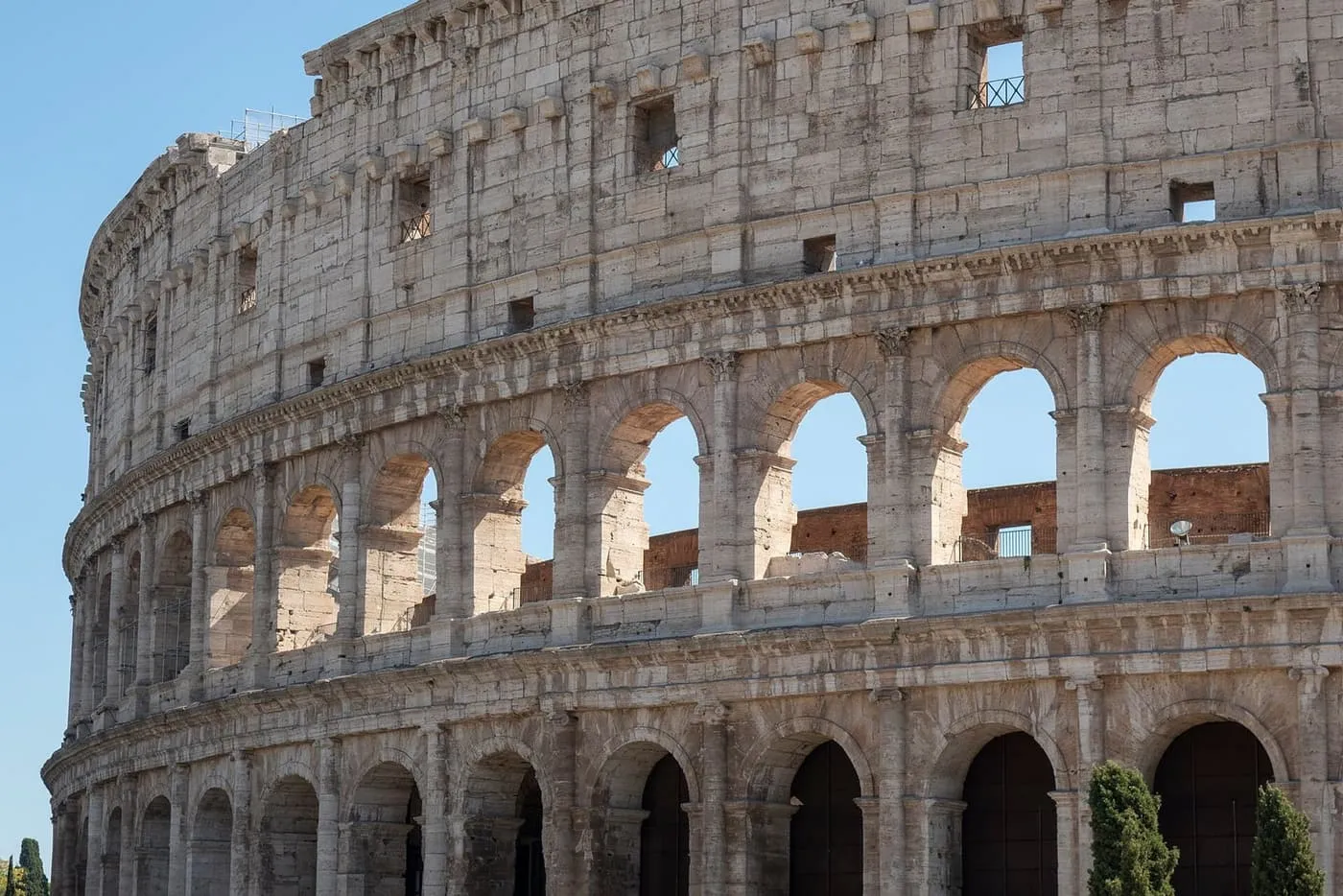 The travertine outer wall of the Colosseum, with tiers of arches against a blue sky