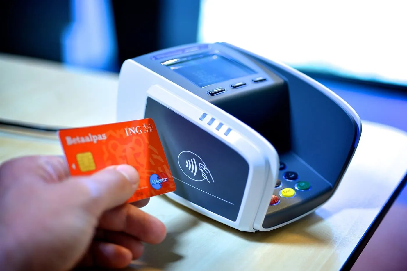 A hand holding a Dutch debit card to a contactless card terminal