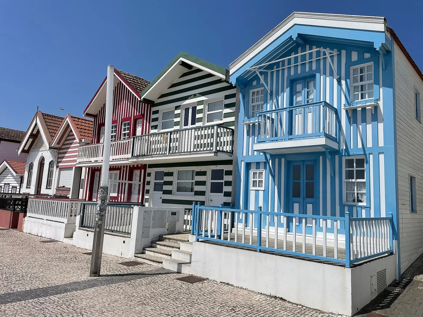Three striped wooden houses in red, green and blue beside a cobbled pavement at Costa Nova
