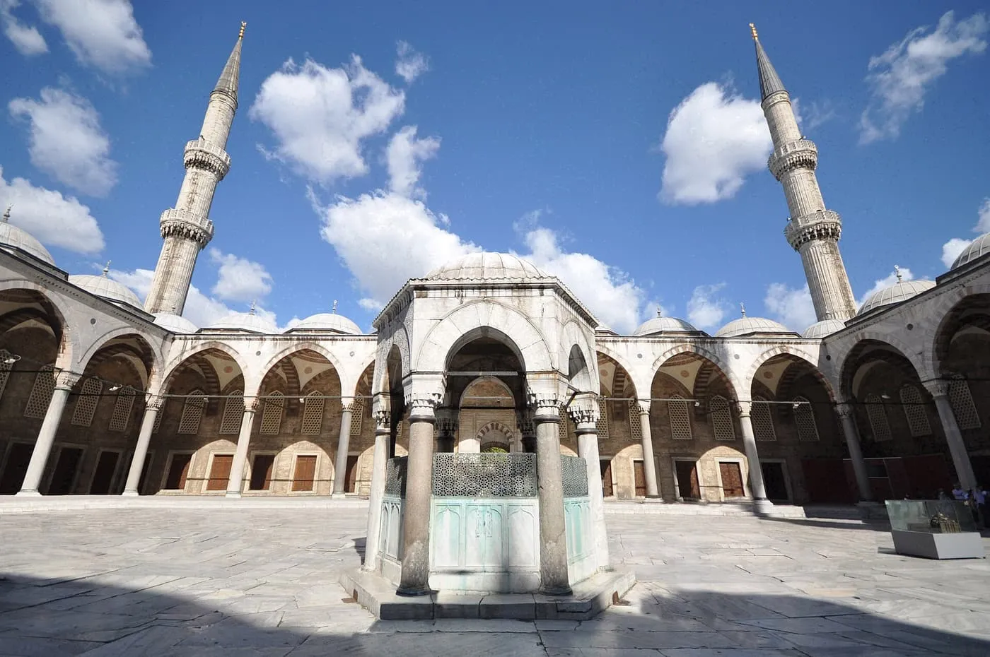 The courtyard of the Blue Mosque: a domed ablution fountain in the centre, arcades around it and two minarets against a blue sky