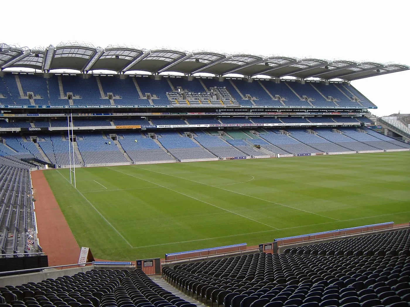 The pitch at Croke Park from the stands, with tiers of blue seats, goalposts and a curved roof over the far side