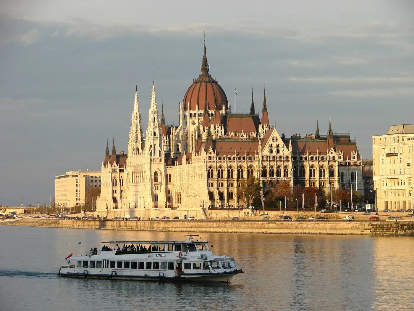 A white Danube sightseeing boat passing below the Hungarian Parliament Building in low evening sun