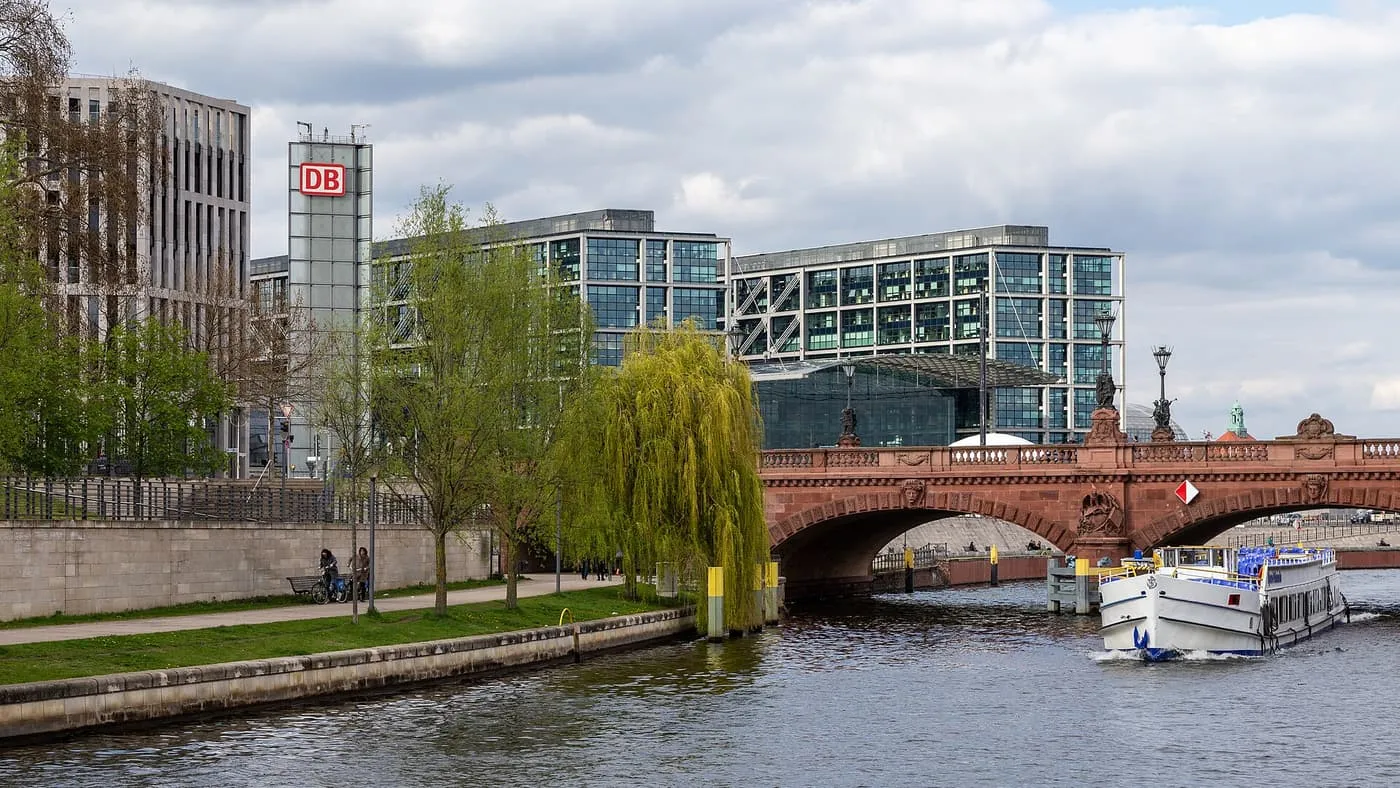 A white cruise boat on the Spree beside the red sandstone Moltke Bridge, with Hauptbahnhof's glass buildings behind