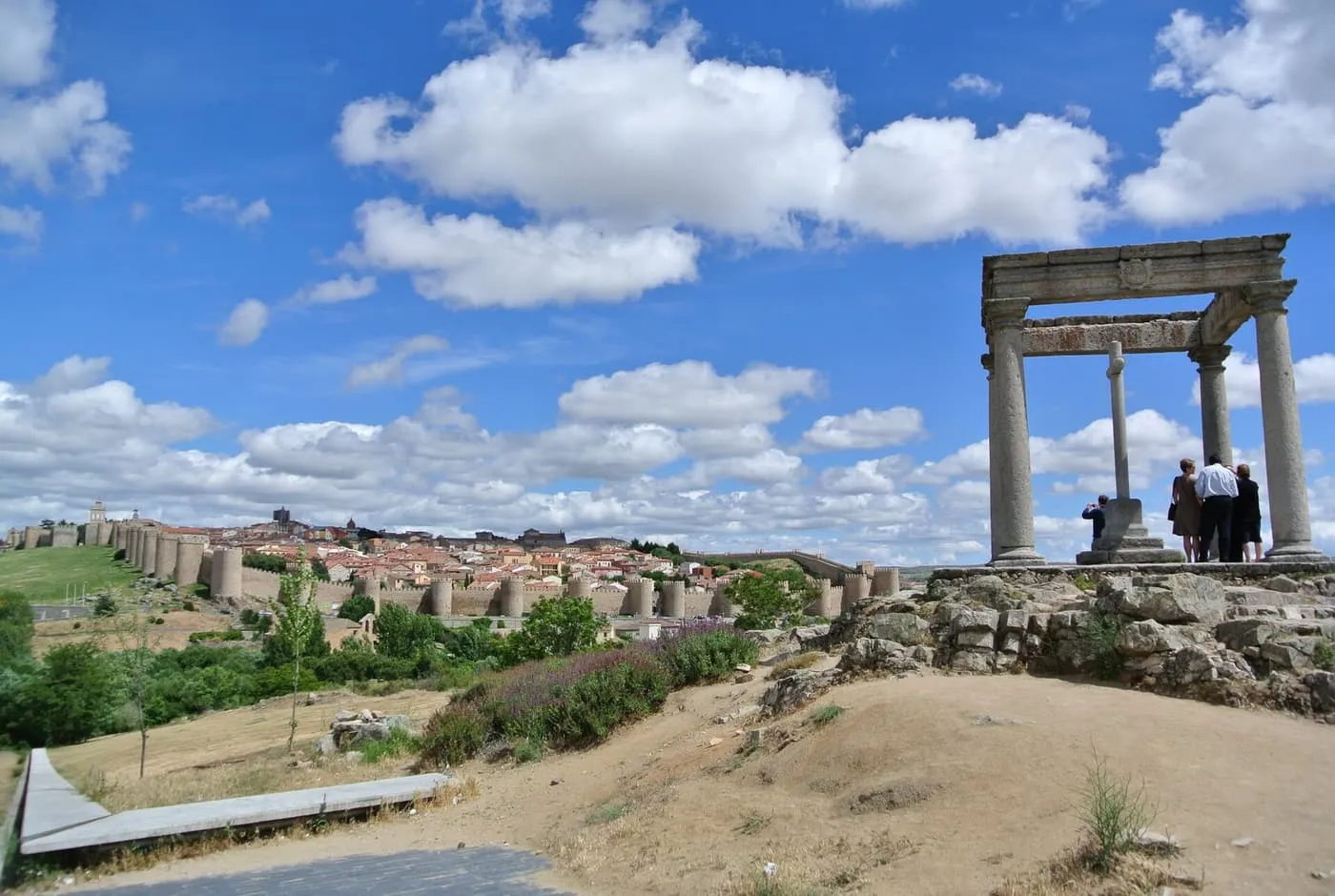 The Cuatro Postes, four granite columns around a cross on a rocky rise, with the walled town of Ávila across the valley