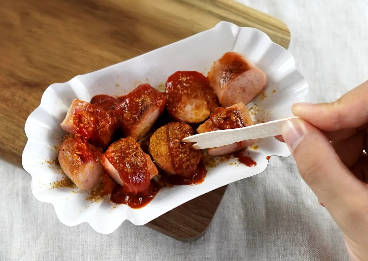 Slices of sausage in a paper tray covered in curry-ketchup sauce and dusted with curry powder, with a wooden fork