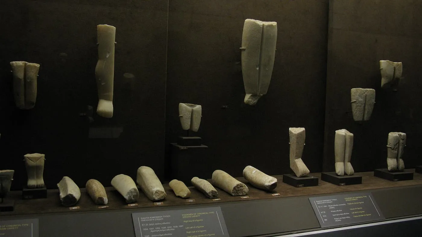 Marble legs and fragments of Cycladic figurines of the canonical type, Spedos variety, on stands in a dark case with labels