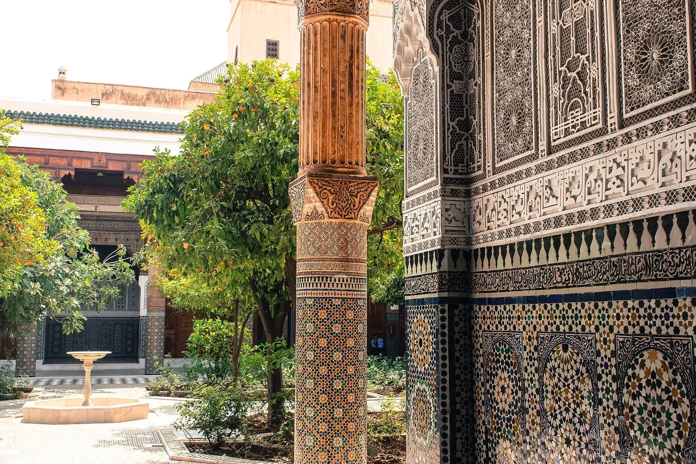 A tiled column and zellige wall in the foreground, looking across an orange-tree courtyard to a fountain at Dar El Bacha